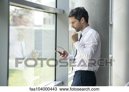 Stock Image - Man using cell phone with hands-free device. Fotosearch