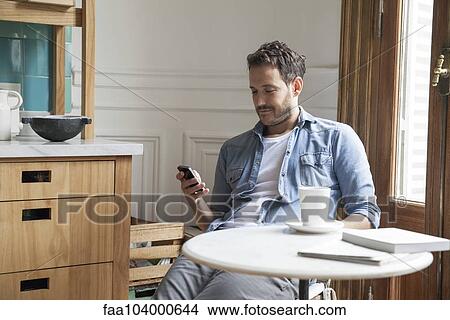 Picture - Man using smartphone at home. Fotosearch