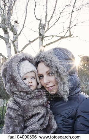 Stock Photograph - Mother holding baby girl outdoors, both wearing winter coats, portrait. Fotosearch