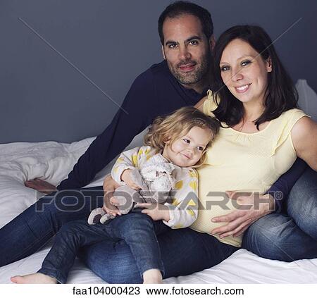 Stock Image - Parents and young daughter sitting together, portrait. Fotosearch