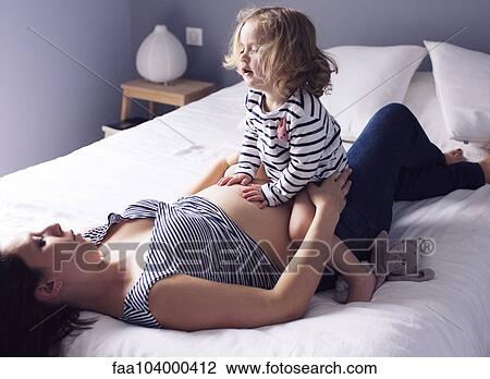 Pregnant mother and young daughter together on bed View Large Photo Image Stock Image - Pregnant mother and young daughter together on bed. Fotosearch