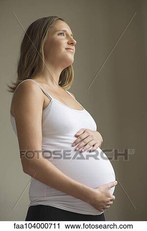 Stock Image - Pregnant woman cradling abdomen. Fotosearch