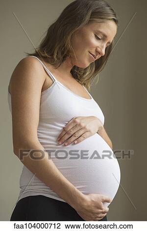 Stock Image - Pregnant woman gazing with affection at her abdomen. Fotosearch