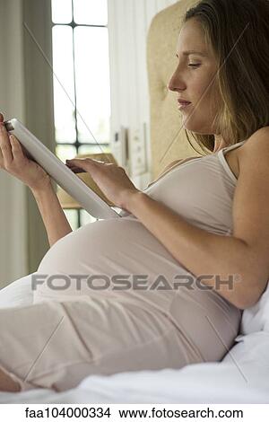 Pregnant woman lying in bed using digital tablet View Large Photo Image Picture - Pregnant woman lying in bed using digital tablet. Fotosearch