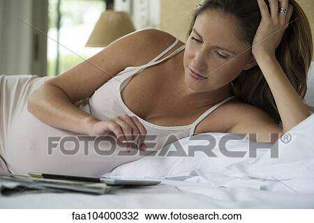 Stock Image - Pregnant woman lying in bed using digital tablet. Fotosearch