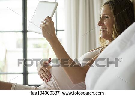 Pregnant woman using digital tablet to video chat with friends and family View Large Photo Image Stock Photo - Pregnant woman using digital tablet to video chat with friends and family. Fotosearch