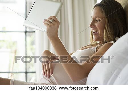 Pregnant woman using digital tablet to video chat with friends and family View Large Photo Image Stock Photo - Pregnant woman using digital tablet to video chat with friends and family. Fotosearch