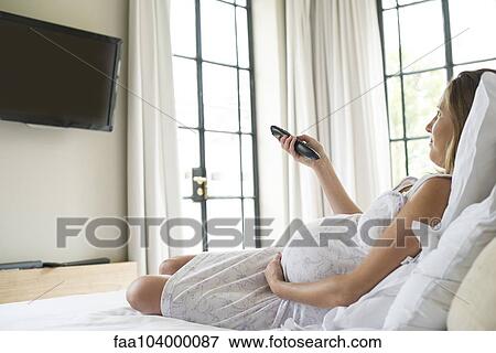 Pregnant woman watching TV on bed View Large Photo Image Stock Photo - Pregnant woman watching TV on bed. Fotosearch