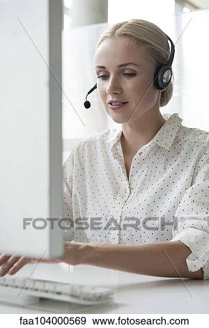 Stock Photo - Woman using desktop computer and headset in office. Fotosearch