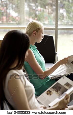 Stock Image - Women reading to kill time in waiting room. Fotosearch