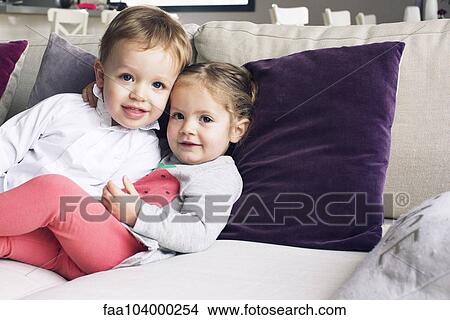 Picture - Young siblings sitting together on sofa, portrait. Fotosearch