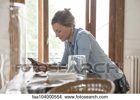 Young woman using smartphone in kitchen View Large Photo Image Picture - Young woman using smartphone in kitchen. Fotosearch