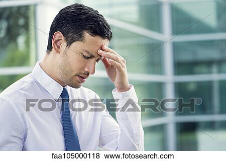 Stock Photo - Businessman holding head and looking down in disappointment. Fotosearch