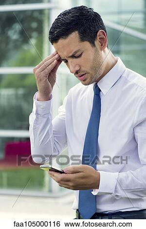 Stock Photograph - Businessman looking at cell phone with worried expression. Fotosearch