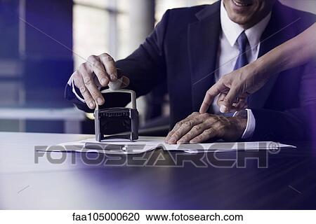 Stock Image - Businessman stamping document with help of assistant. Fotosearch