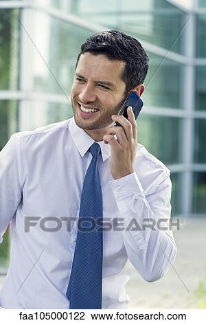 Stock Image - Businessman talking on cell phone and smiling outdoors. Fotosearch