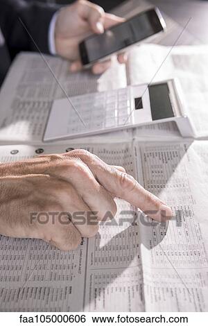 Stock Photograph - Checking stock market performance in newspaper. Fotosearch