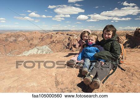 Stock Image - Children sitting at edge of canyon in Canyonlands National Park, Utah, USA. Fotosearch