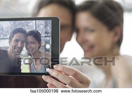Stock Photo - Couple using digital tablet to take a selfie. Fotosearch