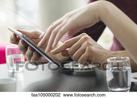 Stock Image - Couple using digital tablet together in cafe, cropped. Fotosearch
