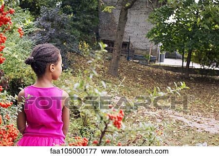 Stock Photo - Girl standing alone outdoors, rear view. Fotosearch