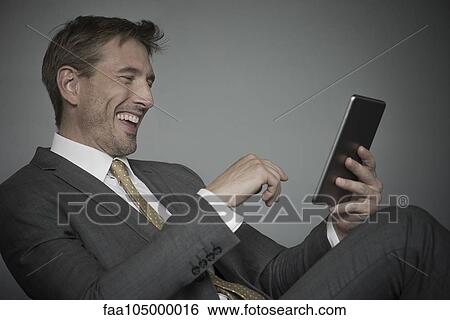 Man laughing while using digital tablet View Large Photo Image Stock Photograph - Man laughing while using digital tablet. Fotosearch