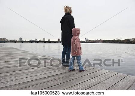 Mother and young daughter standing together on dock, looking at water View Large Photo Image Stock Image - Mother and young daughter standing together on dock, looking at water. Fotosearch