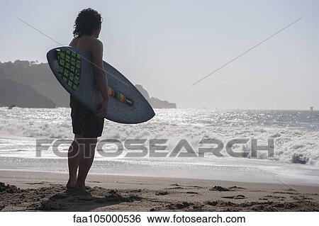 Surfer standing at water's edge, looking at sea View Large Photo Image Stock Photograph - Surfer standing at water's edge, looking at sea. Fotosearch