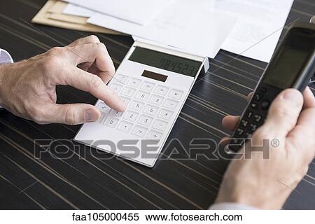 Stock Photography - Using calculator and cell phone. Fotosearch