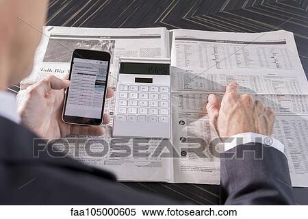 Stock Photography - Using smartphone and newspaper to monitor stock performance. Fotosearch