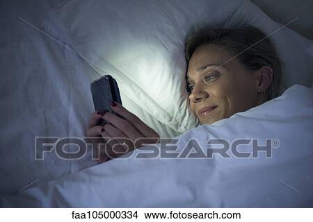 Woman in bed using smartphone View Large Photo Image Picture - Woman in bed using smartphone. Fotosearch