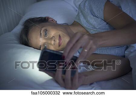 Stock Image - Woman in bed using smartphone. Fotosearch