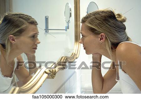 Stock Image - Woman looking at self in bathroom mirror. Fotosearch