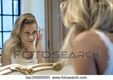 Stock Image - Woman looking bleary-eyed at self in bathroom mirror. Fotosearch