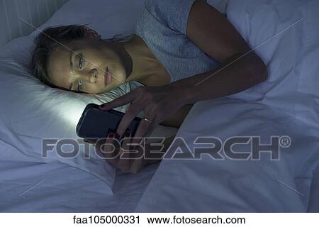 Woman lying in bed using smartphone View Large Photo Image Stock Image - Woman lying in bed using smartphone. Fotosearch