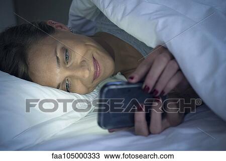 Woman lying in bed using smartphone View Large Photo Image Stock Image - Woman lying in bed using smartphone. Fotosearch