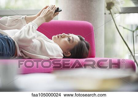 Woman relaxing at home using smartphone View Large Photo Image Picture - Woman relaxing at home using smartphone. Fotosearch