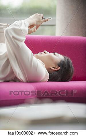 Woman relaxing at home using smartphone View Large Photo Image Stock Photo - Woman relaxing at home using smartphone. Fotosearch