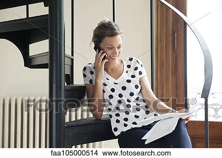 Picture - Woman reviewing document while talking on phone. Fotosearch