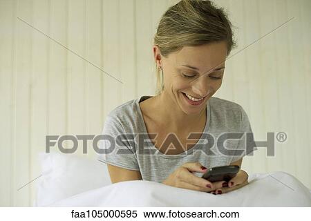 Woman sitting in bed texting View Large Photo Image Stock Photography - Woman sitting in bed texting. Fotosearch