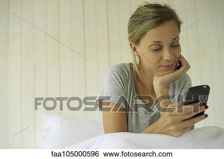 Woman sitting in bed using smartphone View Large Photo Image Stock Photograph - Woman sitting in bed using smartphone. Fotosearch