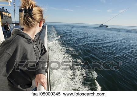 Stock Photography - Woman standing on deck of ferry boat, looking over shoulder at view. Fotosearch