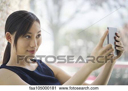 Stock Image - Woman taking a photo using a digital tablet. Fotosearch