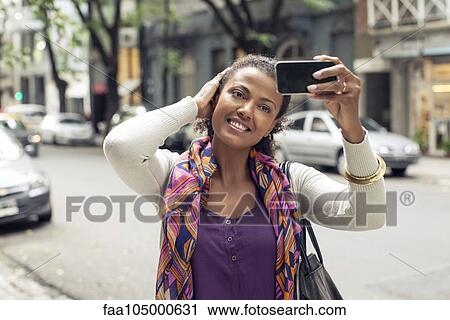 Stock Image - Woman taking selfie on street. Fotosearch