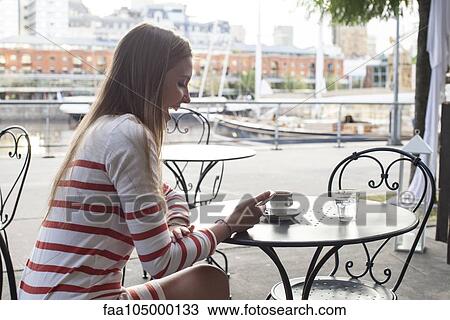 Young woman sitting at sidewalk cafe, laughing at smartphone View Large Photo Image Stock Image - Young woman sitting at sidewalk cafe, laughing at smartphone. Fotosearch