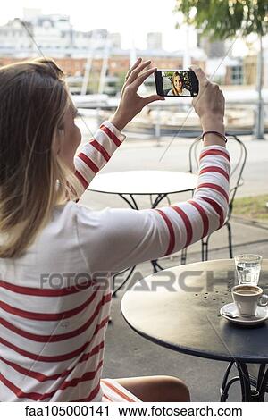 Stock Image - Young woman taking a selfie at sidewalk cafe. Fotosearch