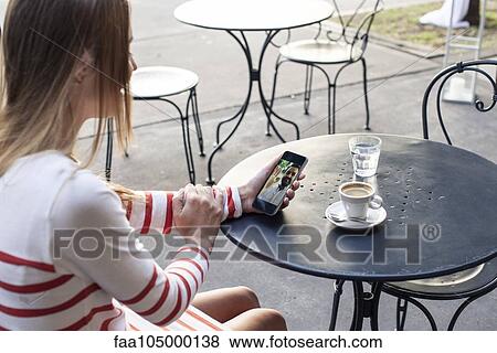 Stock Photo - Young woman using multimedia smartphone in outdoor cafe. Fotosearch