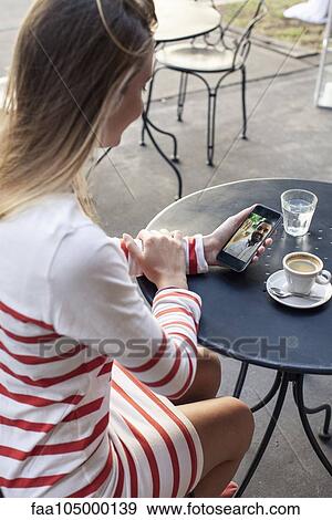 Young woman using multimedia smartphone at outdoor cafe View Large Photo Image Stock Photo - Young woman using multimedia smartphone at outdoor cafe. Fotosearch
