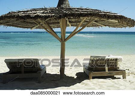 Beach chairs shaded by thatched umbrella View Large Photo Image Stock Image - Beach chairs shaded by thatched umbrella. Fotosearch