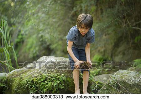 Boy bending over to pick up large wet rock View Large Photo Image Stock Image - Boy bending over to pick up large wet rock. Fotosearch